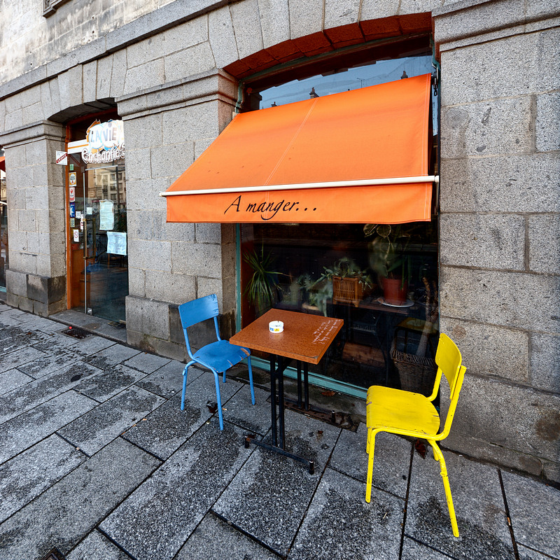 un restaurant avec un store orange, une chaise bleue et une chaise jaune